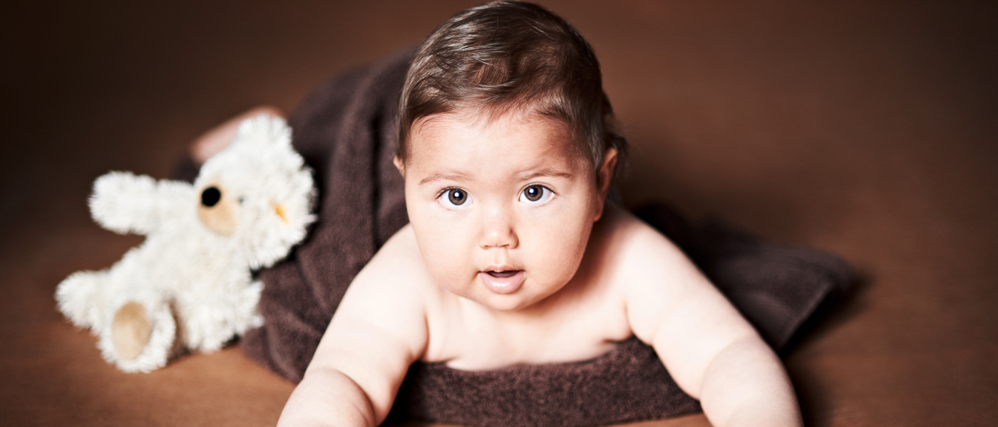 Portraitfoto eines Babies mit brauner Decke und Teddybär.
